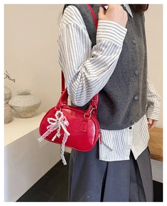 Close-up of a red Boston bag featuring a pearl bow, lace ribbon, and heart charm detail