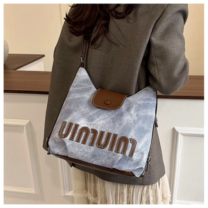 Detail der blau-weißen Canvas-Tasche mit braunen Leder-Patches und Schriftzug-Element
