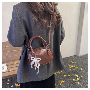 Detailed view of brown leather bag with pearl lace bow charm in a warm autumn street scene