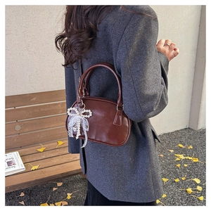 Close-up of brown leather bowling bag with pearl bow pendant in an autumn setting