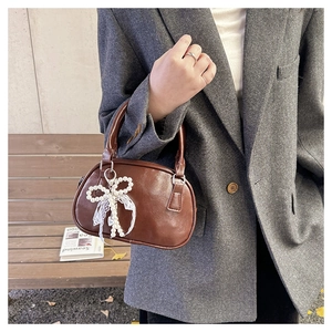 Detail of brown PU bowling bag with pearl bow and lace charm on a grey blazer background