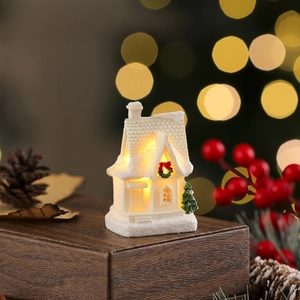Close-up of a miniature resin snow house with warm LED glow and Christmas decor
