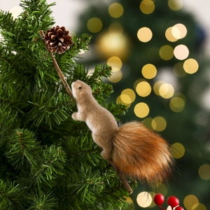 Close-up of squirrel ornament with pine cone on a branch against a festive bokeh background
