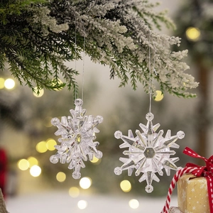 Close-up of clear acrylic snowflake ornaments hanging on snowy pine branches with bokeh lights