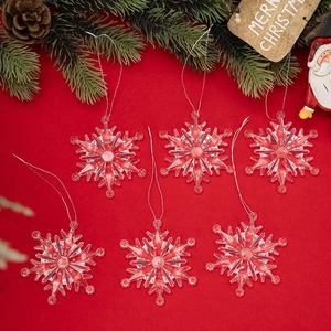 Close-up of six clear acrylic snowflakes with silver strings on a red festive background