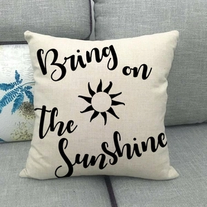 Beige linen pillow cover with Bring on the Sunshine print on a grey sofa