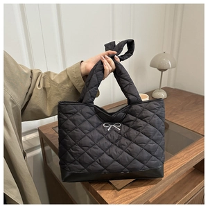 Detail of black quilted tote bag featuring silver bow accent and durable leather base trim