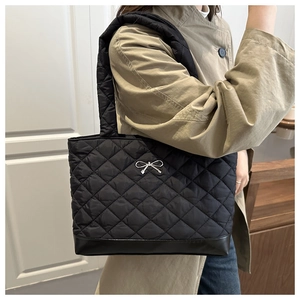 Detail view of black quilted tote bag featuring silver metal bow and durable leather base
