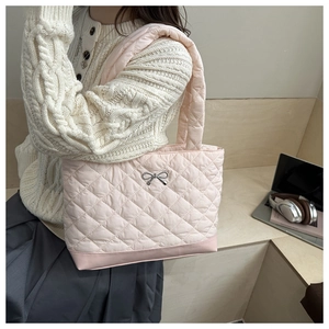 Detailed close-up of pink quilted tote bag with silver bow buckle on indoor background