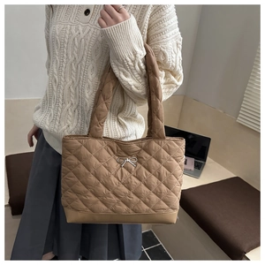 Detailed view of brown quilted tote bag with silver bow charm and soft padded texture