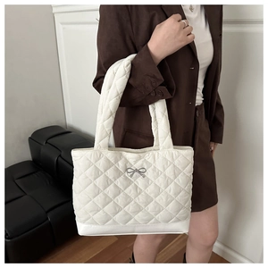 Close-up of white quilted tote bag with silver metal bow detail and wide padded handle