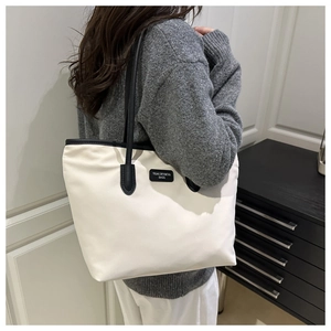 Detail of minimalist cream tote bag featuring black leather trim and branded logo tag
