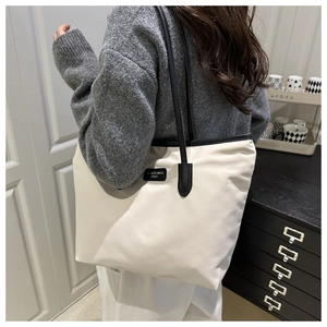 Detail of off-white tote bag with black straps and Tenderness logo shown on model