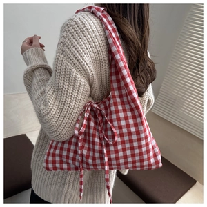 Detail of red gingham canvas shoulder bag with decorative side bow on a beige sweater