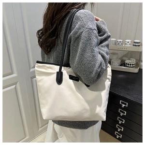 Detail of a large beige tote bag with black leather straps worn by a model in a home setting