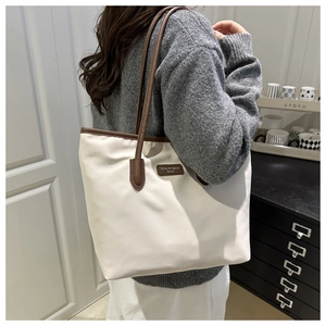 On-shoulder view of large cream tote bag with brown leather straps and logo patch