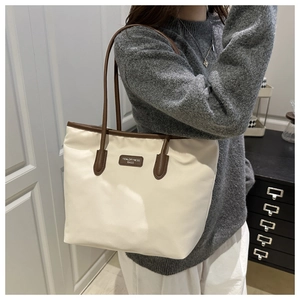Detail view of large white nylon tote bag with brown leather handles and brand label