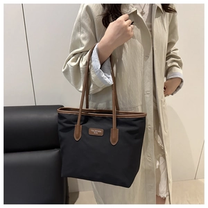 Detailed view of black tote bag with brown leather handles and brand logo patch