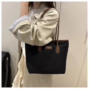 Detail of black large capacity tote bag with brown leather handles and brand label
