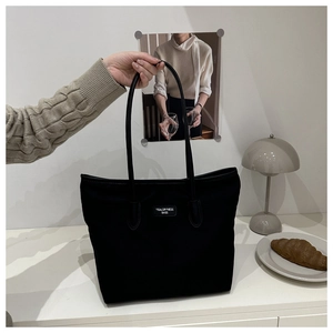 Detail showing a large black canvas tote bag with slim shoulder straps and a white logo label
