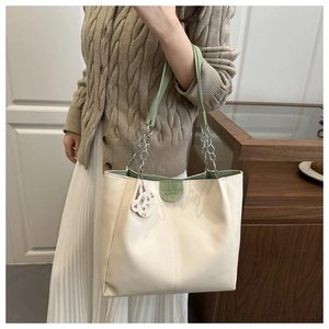 Detailed close-up of cream tote bag with green handles and white cat charm on its strap