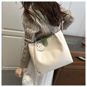Detail of cream tote bag with green handles, silver chain and tiger charm on a model