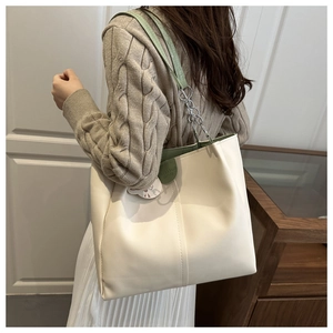 Detail of cream tote bag with green leather straps and silver chain in a minimal setting