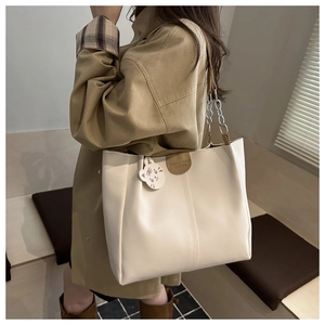 Detail view of large beige tote bag with chain strap and cute white cat charm