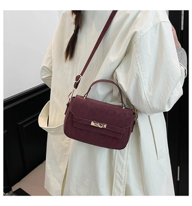 Détail du sac bandoulière en cuir bordeaux texturé avec poignée dorée et fermoir rotatif