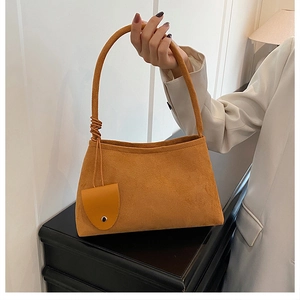 Detail of caramel suede underarm bag featuring knotted handle and round charm
