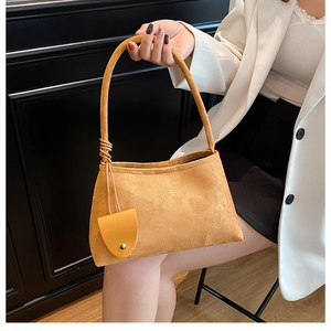 Detail of yellow suede underarm bag featuring a unique knotted strap and metal buckle charm