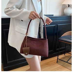 Detail of burgundy faux suede hobo bag with leather accessory held by model