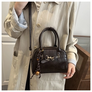 Detail of dark brown Boston bag with golden horsebit buckle and woven charm