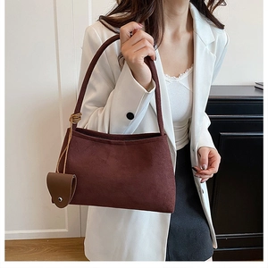 Detail of dark brown suede shoulder bag with knotted strap and small round accessory