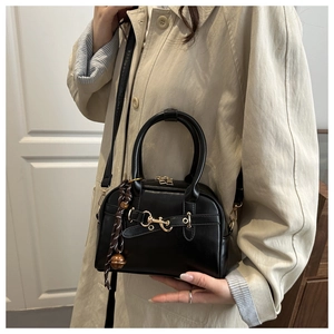 Detail of black faux leather shell bag featuring golden horsebit and woven bell charm