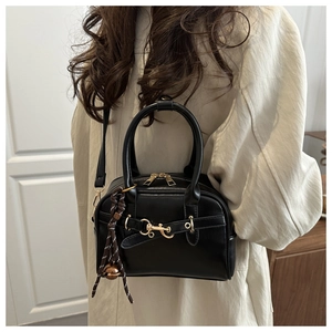 Detail of black leather shell bag with gold hardware and woven pendant on model