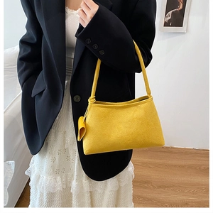 Detail of yellow faux suede underarm bag with a hanging leather charm and slim handle