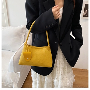 Detail of a vibrant yellow suede underarm bag with small pouch charm on a model