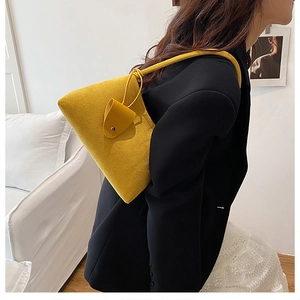 Detailed view of yellow suede shoulder bag worn by model showing minimalist triangle design