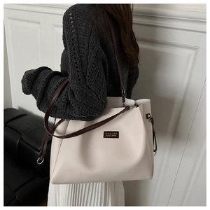 Detalle del bolso tote crema grande con correas marrones y logo sobre acabado cuero