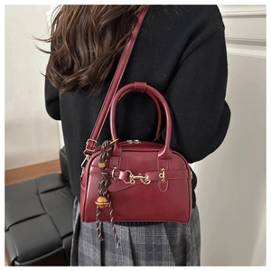 Close-up of vintage burgundy shell bag with gold hardware worn by a model in a sweater