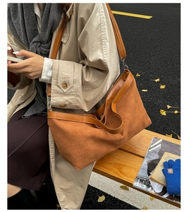 Detail of a large brown matte suede tote bag shown on a model in a cozy outdoor setting