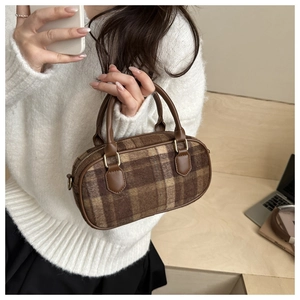 Detail of wool shell bag featuring brown plaid pattern and leather handles on wooden desk