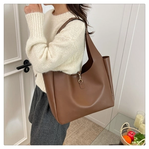 Detail of dark brown leather tote bag showing wide shoulder strap and metal hook buckle