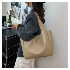 Detail of khaki leather tote bag featuring a gold metal hook closure and textured finish