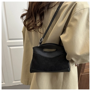 Detail of black quilted suede handbag with adjustable strap worn with khaki trench coat