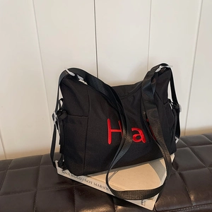 Sac en nylon noir avec broderie Hai rouge et bandoulière réglable sur tabouret en cuir