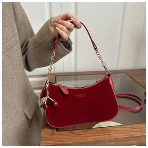 Détail du sac bandoulière en daim rouge avec chaîne dorée et pendentif cerise chic