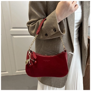 Détail du sac en daim rouge avec chaîne dorée et breloque cerise sur blazer beige