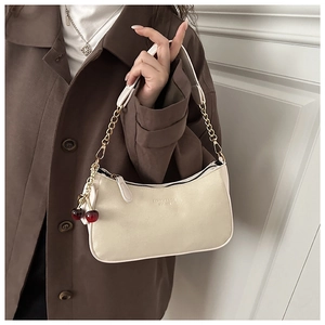 Détail du sac croissant crème avec bandoulière en chaîne dorée et breloque cerise